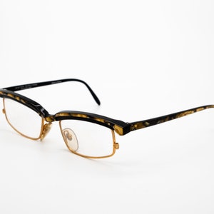 May include: Black and gold-toned eyeglasses with a tortoiseshell pattern on the arms. The glasses have a semi-rimless design with gold metal frames.