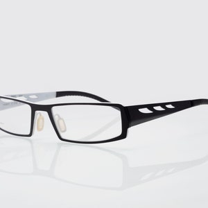 Könnte beinhalten: Schwarze und weiße rechteckige Brille mit einem dünnen, schwarzen Rahmen und einem weißen Akzent auf der Oberseite des Rahmens.