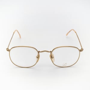 Op de afbeelding: Goudkleurige bril met ovale glazen. De monturen en veren zijn warm goudkleurig en de glazen zijn helder. De bril staat tegen een effen witte achtergrond. Het ontwerp is klassiek en ingetogen.