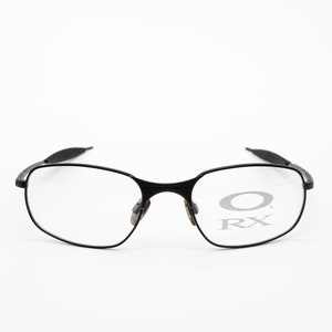 K&ouml;nnte beinhalten: Schwarze Metallgestellbrille mit klaren Gl&auml;sern. Das Oakley-Logo und RX sind auf den Gl&auml;sern sichtbar.