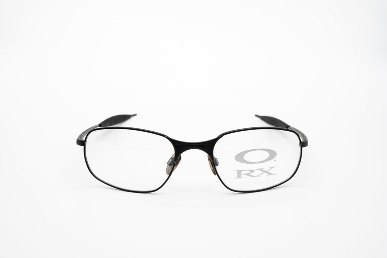 K&ouml;nnte beinhalten: Schwarze Metallgestellbrille mit klaren Gl&auml;sern. Das Oakley-Logo und RX sind auf den Gl&auml;sern sichtbar.