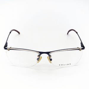 Könnte beinhalten: Randlose Brille mit dunkelblauem Rahmen und braunen Bügeln. Die Gläser sind klar, und der Markenname "CELINE" ist auf dem rechten Glas aufgedruckt. Die Brille hat ein minimalistisches Design.