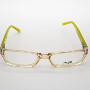 May include: A pair of clear, rectangular eyeglasses with green arms. The brand name "AUS" is printed on the right lens.