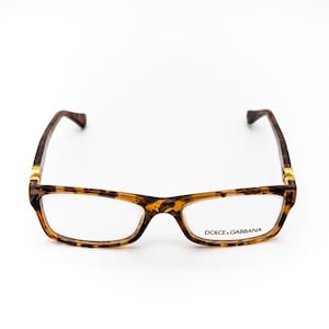 Op de afbeelding: Rechthoekige bril met een montuur met schildpadpatroon. De heldere glazen zitten in een bruin en geel montuur met gouden details. De merknaam Dolce & Gabbana is op het rechterglas gedrukt.