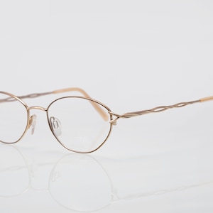 Könnte beinhalten: Goldfarbene Metallbrille mit einem verdrehten Drahtbügel und ovalen Gläsern.