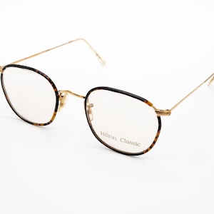 May include: Gold-rimmed glasses with tortoiseshell frames. The glasses have clear lenses and the words "Hilton Classic" are printed on the right lens.