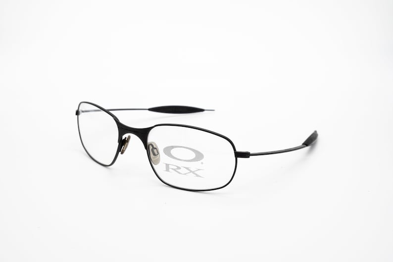 K&ouml;nnte beinhalten: Schwarze Metallgestellbrille mit klaren Gl&auml;sern. Der Markenname "Oakley RX" ist auf dem rechten Glas sichtbar.