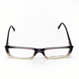 May include: Giorgio Armani eyeglasses with a rectangular frame. The frame is a gradient of gray and clear, with dark gray temples. The brand name is printed on the right lens.