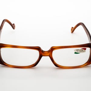 May include: Tortoiseshell eyeglasses with a rectangular frame and clear lenses. The brand name "Tlook Milano" is printed on the right lens.