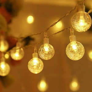 May include: String of warm white LED globe lights. Each clear globe has a textured surface and contains a bright, warm light. The lights are strung on a thin, silver wire, creating a festive and decorative lighting option.