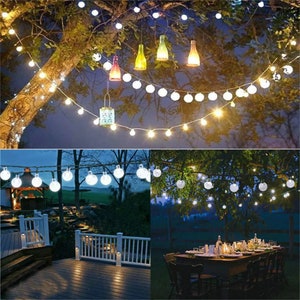 Puede incluir: Luces de cadena para exteriores con bombillas redondas blancas y un brillo blanco c&aacute;lido, colgadas de las ramas de los &aacute;rboles. La imagen tambi&eacute;n muestra botellas de vidrio decorativas y una linterna colgando del &aacute;rbol, creando un ambiente festivo.