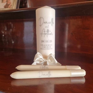 May include: White wedding unity candles with the names Danielle and Arthur, the date 20/11/25, and the location Gracehill Church Ballymena.