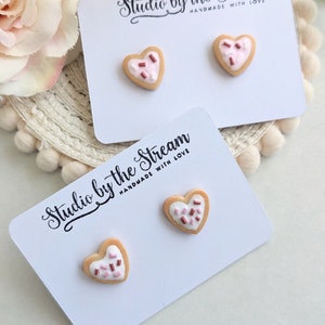 Puede incluir: Dos pares de pendientes de galleta en forma de coraz&oacute;n con chispas rosas y marrones en una tarjeta blanca con el texto "Studio by the Stream Handmade with Love".