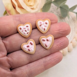 Puede incluir: Cuatro galletas en forma de coraz&oacute;n con chispas rosas y marrones en la parte superior. Las galletas est&aacute;n en una mano.