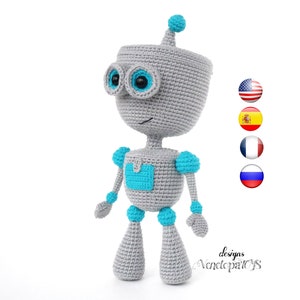 May include: A gray crocheted robot toy with blue accents. The robot has a smiling face with blue eyes and a small antenna on its head. The robot is standing on a white background.