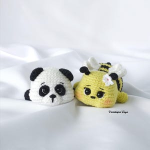 Puede incluir: Dos juguetes de ganchillo hechos a mano: un oso panda y una abeja. El panda es blanco con orejas y parches oculares negros. La abeja es amarilla con rayas negras, alas blancas y una pequeña flor. Los juguetes están sobre una superficie blanca.
