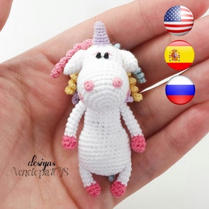 May include: A small white crocheted unicorn with pink hooves, a purple horn, and a rainbow mane. The unicorn is being held in a hand.
