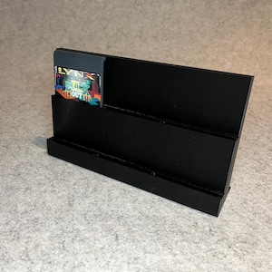 May include: Black plastic stand with three tiers for displaying video game cartridges. A Lynx cartridge with the game "Blue Lightning" is displayed in the top tier.