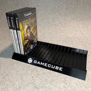 May include: Black GameCube game holder with the GameCube logo and text. Three Harry Potter GameCube game cases are displayed in the holder. The game cases are black with white text and a colorful image of Harry Potter.