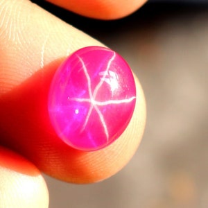 May include: A pink star ruby gemstone with a six-pointed star in the center.