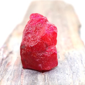 Op de afbeelding: Een grote, ruwe, rode robijn edelsteen. De robijn ligt op een lichtbruin houten oppervlak.
