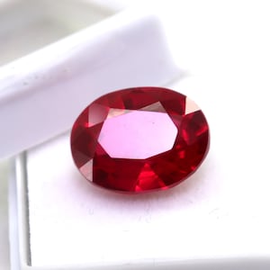 Op de afbeelding: Een dieprode ovale edelsteen in een witte doos.