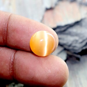 May include: A round, orange-colored gemstone with a cat's eye effect. The gemstone is smooth and polished.