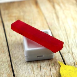 Peut inclure: Un bâtonnet de peinture aquarelle rouge dans un récipient en plastique blanc. Le récipient a une petite indentation sur le dessus.