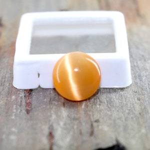 May include: A round, orange cat's eye gemstone with a white sheen.
