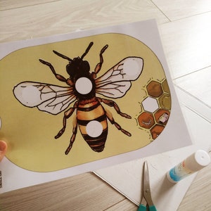 Puede incluir: Una plantilla de artesan&iacute;a imprimible con una abeja de dibujos animados con c&iacute;rculos blancos en su cuerpo. La abeja est&aacute; sobre un fondo amarillo con un patr&oacute;n de panal en la esquina.
