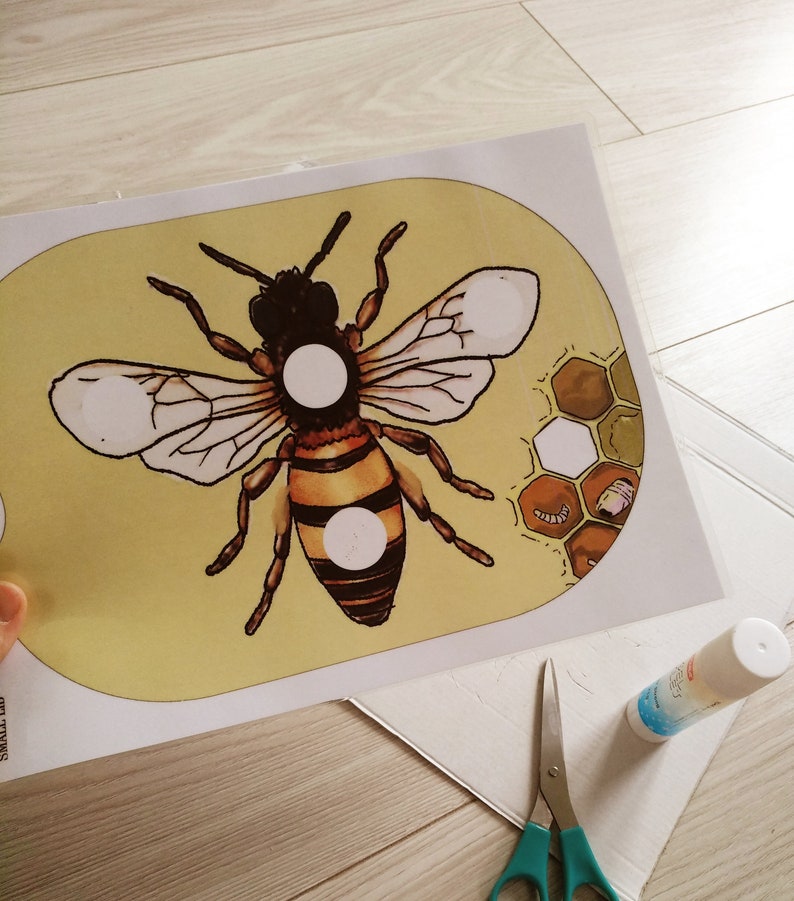 Puede incluir: Una plantilla de artesan&iacute;a imprimible con una abeja de dibujos animados con c&iacute;rculos blancos en su cuerpo. La abeja est&aacute; sobre un fondo amarillo con un patr&oacute;n de panal en la esquina.