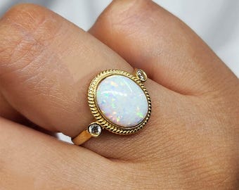 May include: A gold ring with a white opal gemstone and two smaller clear gemstones. The ring is on a person's finger.