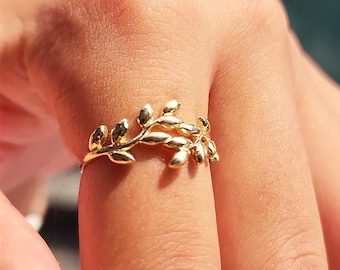Puede incluir: Un anillo de oro con un delicado diseño de hojas. El anillo se lleva en un dedo.