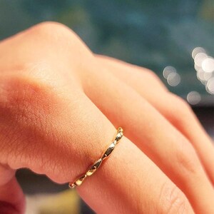 Op de afbeelding: Een gouden ring met een gedraaid ontwerp. De ring zit aan een vinger.