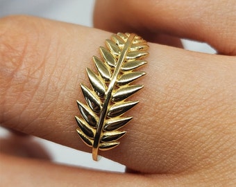 Puede incluir: Un anillo de oro con un diseño de hoja. El anillo está hecho de una sola pieza de metal y tiene un acabado liso.
