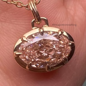 Può includere: Una collana color oro con un pendente ovale in pietra preziosa rosa chiaro. Il pendente è incastonato in una lunetta dorata e appeso a una sottile catena d'oro. La collana è mostrata su uno sfondo neutro.