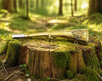 May include: A brass hunting horn with a silver mouthpiece rests on a moss-covered tree stump in a forest setting. The horn features an engraved animal emblem and is designed with a curved shape. The background shows a blurred forest.