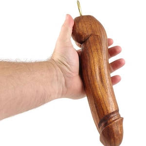 May include: A carved wooden object with a dark brown finish, held in a hand. The object has a rounded top with a brass loop and a cylindrical body with carved details. The wood grain is visible.