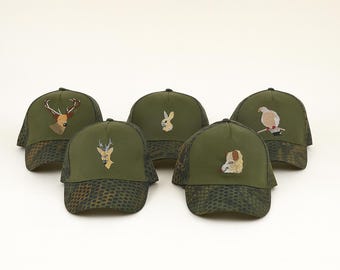 May include: Five olive green baseball caps with embroidered animal designs. The caps feature a camouflage pattern on the bill and a mesh back. The embroidered animals include a deer, rabbit, bird, and dog.