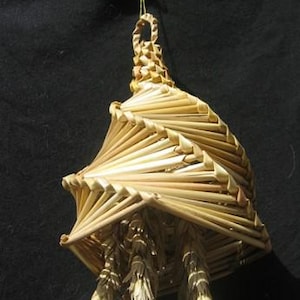 May include: A straw ornament shaped like a house with a spiral roof and wheat stalks hanging from the bottom.