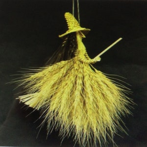 May include: A handcrafted witch figurine made from dried wheat stalks. The witch wears a pointed hat and holds a small broom. The figure has long, flowing hair and a full skirt, all made from the same golden-brown wheat.