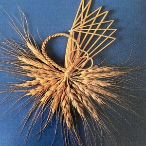 Peut inclure: Une gerbe de blé dorée liée avec un motif de paille tissée. La gerbe est disposée en éventail avec les extrémités des épis de blé étalés.