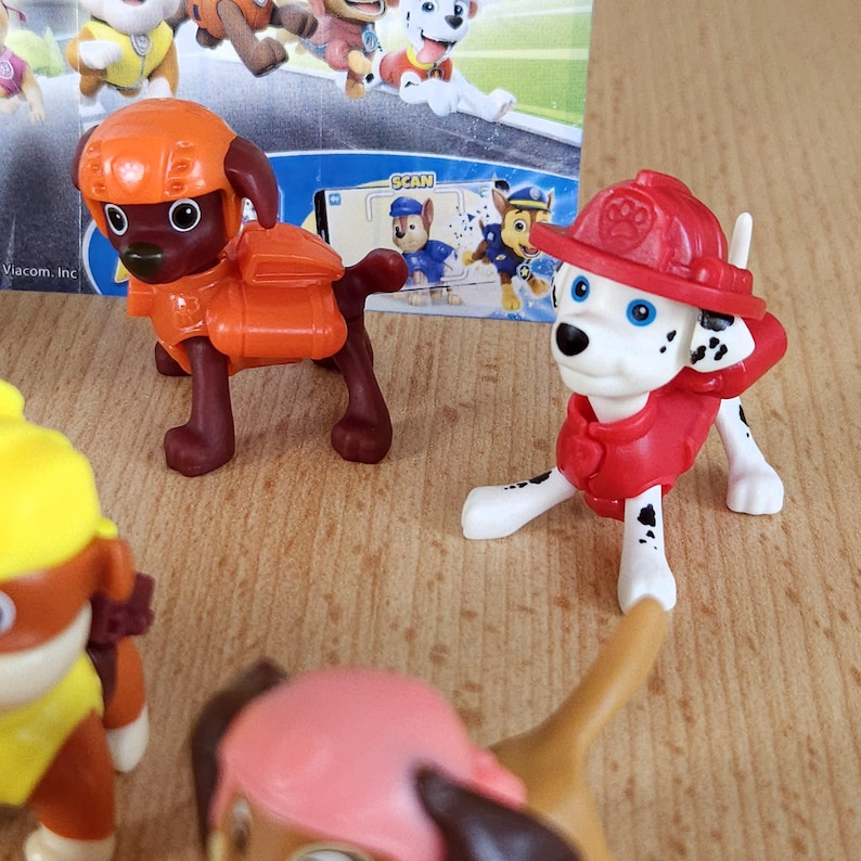 May include: A set of six Paw Patrol character figurines. The figurines are made of plastic and are painted in bright colors. The characters include Chase, Marshall, Skye, Rubble, Rocky, and Zuma. The figurines are all wearing their signature uniforms and accessories. The figurines are posed in various action poses. The figurines are all approximately 2 inches tall.