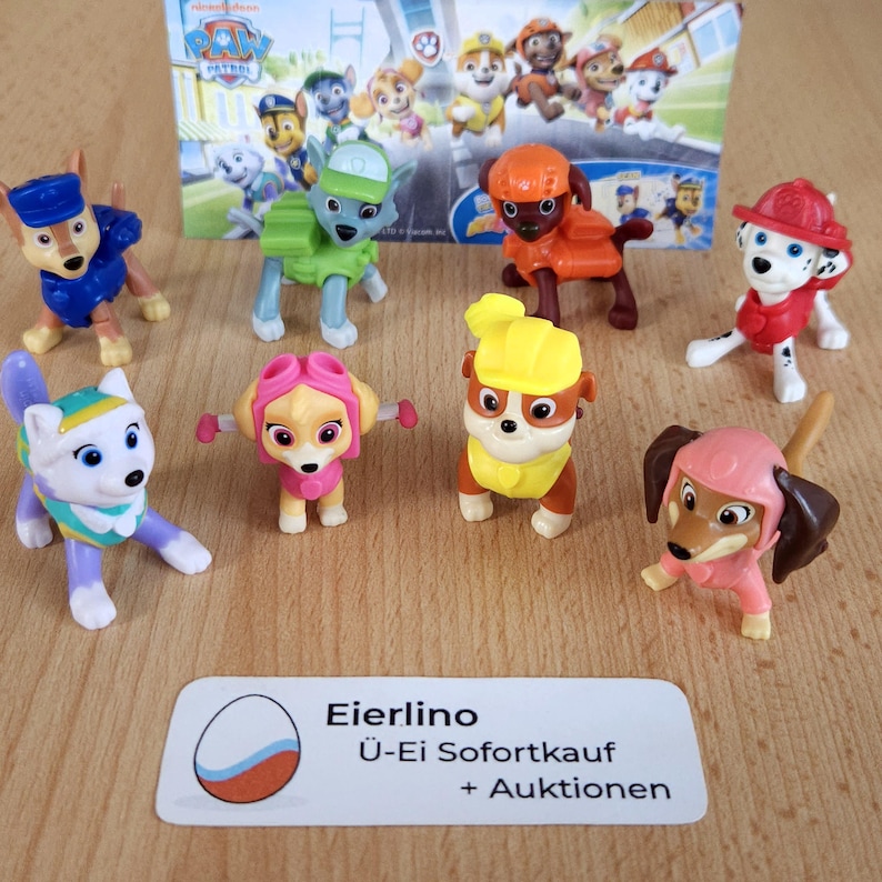 May include: A set of eight Paw Patrol character figurines. The figurines are made of plastic and are painted in bright colors. The characters include Chase, Marshall, Skye, Rubble, Rocky, Zuma, Everest, and Tracker. The figurines are all in different poses and are standing on a wooden surface. The text "Eierlino &Uuml;-Ei Sofortkauf + Auktionen" is visible in the lower right corner of the image.