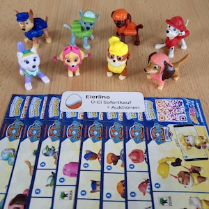 May include: Eight small plastic figurines of characters from the animated television series Paw Patrol. The characters include Chase, Marshall, Skye, Rubble, Rocky, Zuma, Everest, and Tracker. The figurines are all in different poses and are wearing their signature uniforms. The figurines are arranged in a circle on a white surface. The text "Eierlino &Uuml;-Ei Sofortkauf + Auktionen" is visible on a white label.