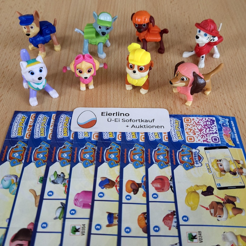 May include: Eight small plastic figurines of characters from the animated television series Paw Patrol. The characters include Chase, Marshall, Skye, Rubble, Rocky, Zuma, Everest, and Tracker. The figurines are all in different poses and are wearing their signature uniforms. The figurines are arranged in a circle on a white surface. The text "Eierlino &Uuml;-Ei Sofortkauf + Auktionen" is visible on a white label.