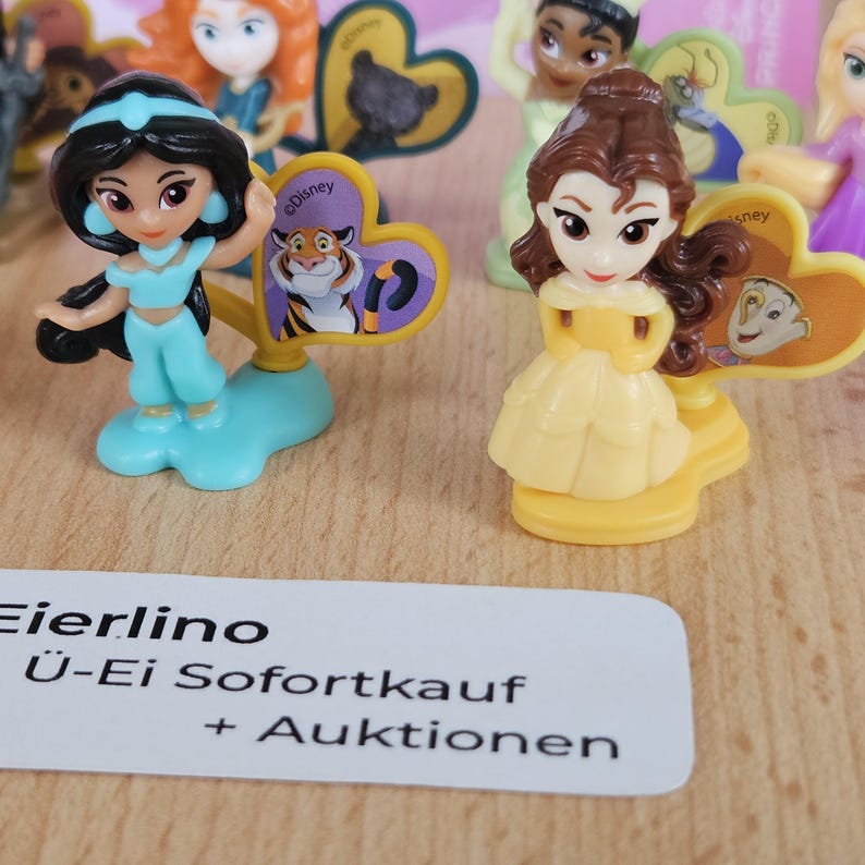 May include: Two small plastic figurines of Disney princesses, Jasmine and Belle, with their respective cartoon characters on the base. Jasmine is wearing a blue outfit and Belle is wearing a yellow dress.