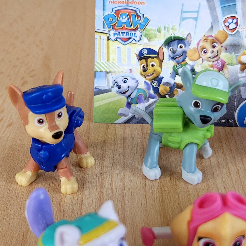 May include: A set of six Paw Patrol character figurines. The figurines are made of plastic and are painted in bright colors. The characters include Chase, Marshall, Skye, Rocky, Zuma, and Rubble. The figurines are all wearing their signature uniforms and accessories. The figurines are packaged in a cardboard box with a Paw Patrol logo.