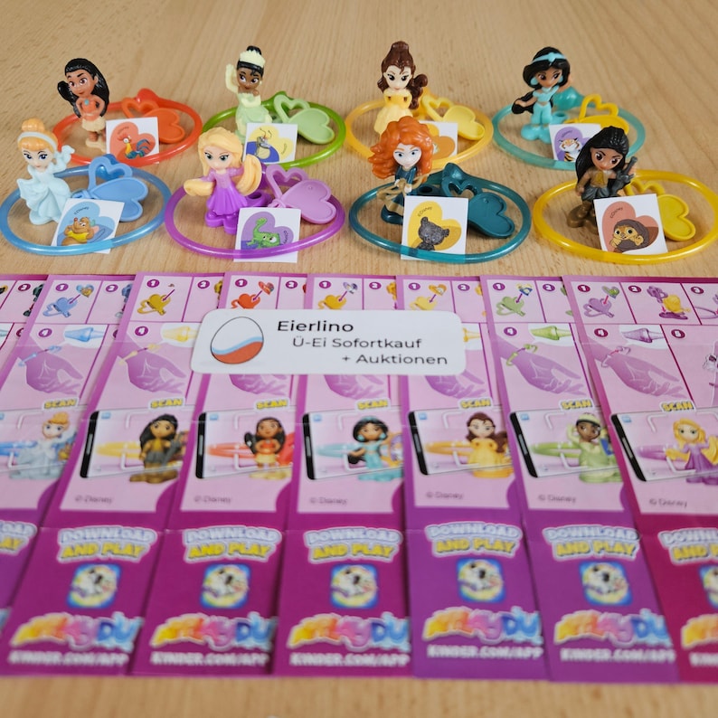 May include: Eight colorful plastic rings with Disney Princess figurines attached. Each ring has a heart-shaped charm with a princess image. The rings are displayed on a wooden surface with pink and white cards that say "Download and Play" and "Kinder.com/app".
