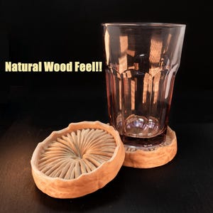 May include: Two natural wood coasters with a circular design. The coasters are made of light brown wood and have a raised centre. A clear glass with a pink tint is sitting on top of the coasters. The text "Natural Wood Feel!!" is written in yellow letters on a black background.